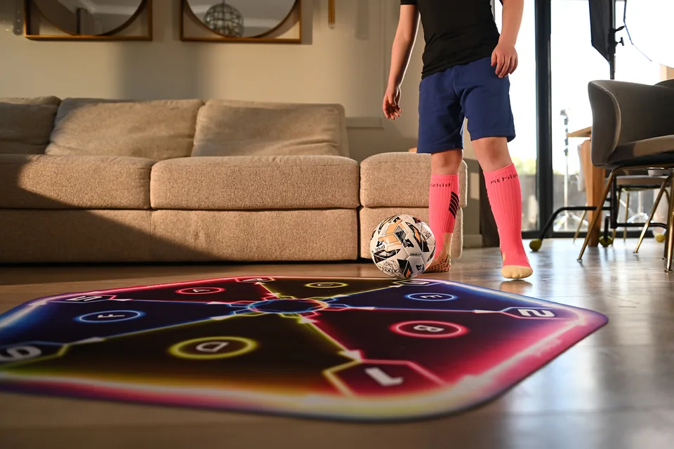 A young football player preparing to train with a ball on the IQ360 mat at home